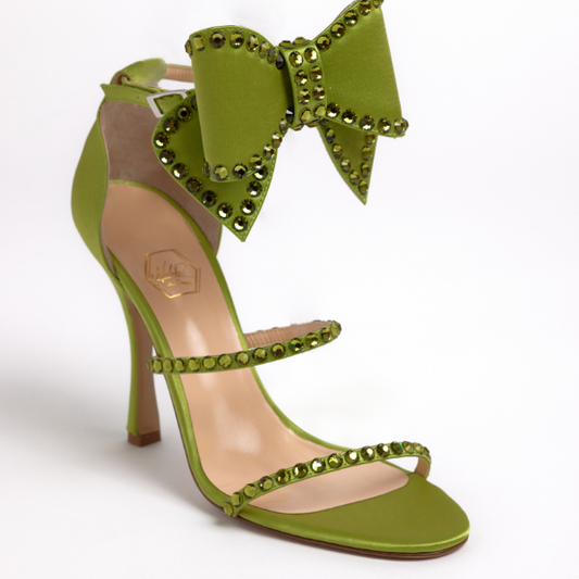 A green satin sandal featuring a deconstructed bow ankle strap with crystal details and a high heel.